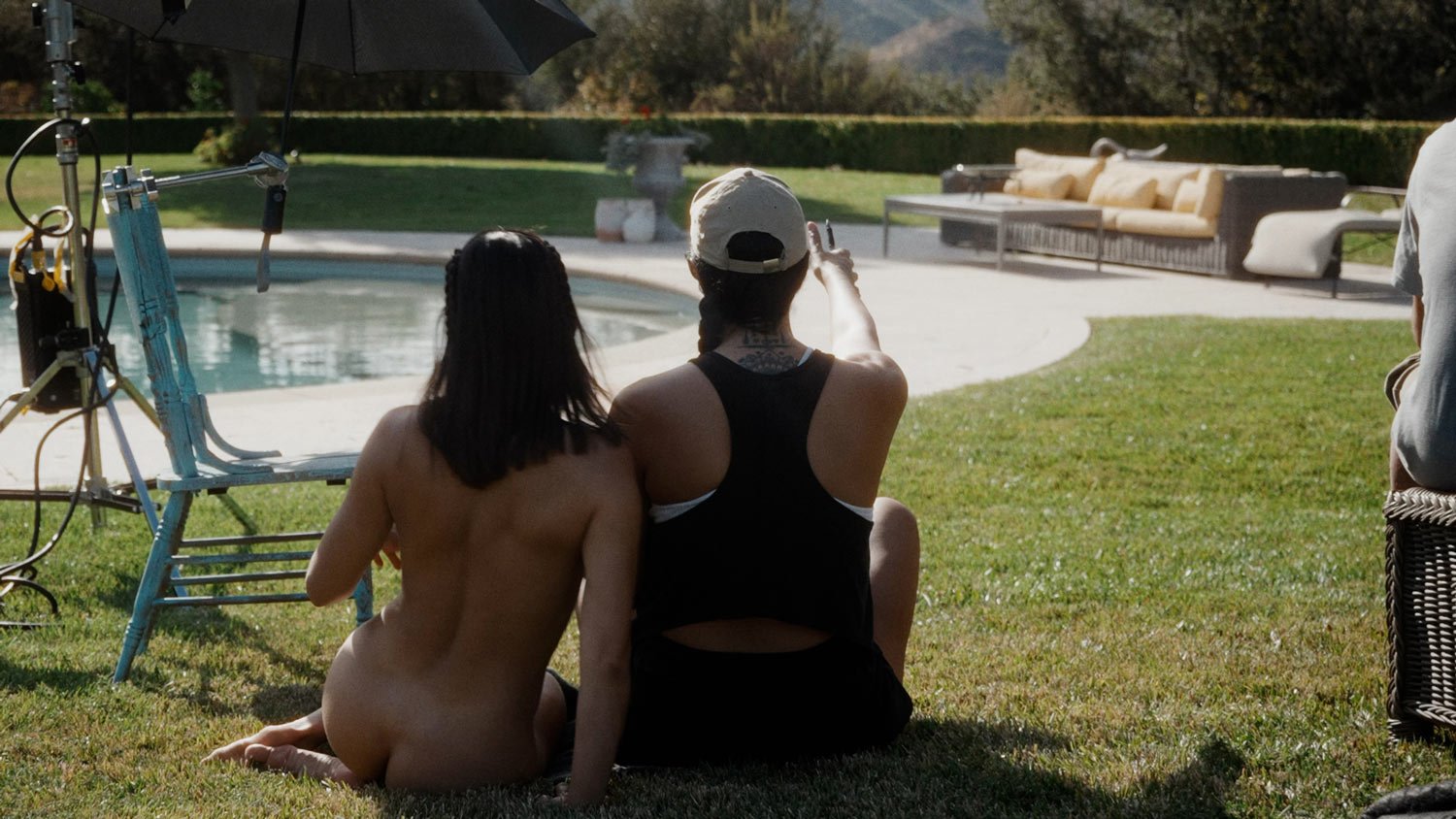 two woman sitting next to each other by a pool, one is naked