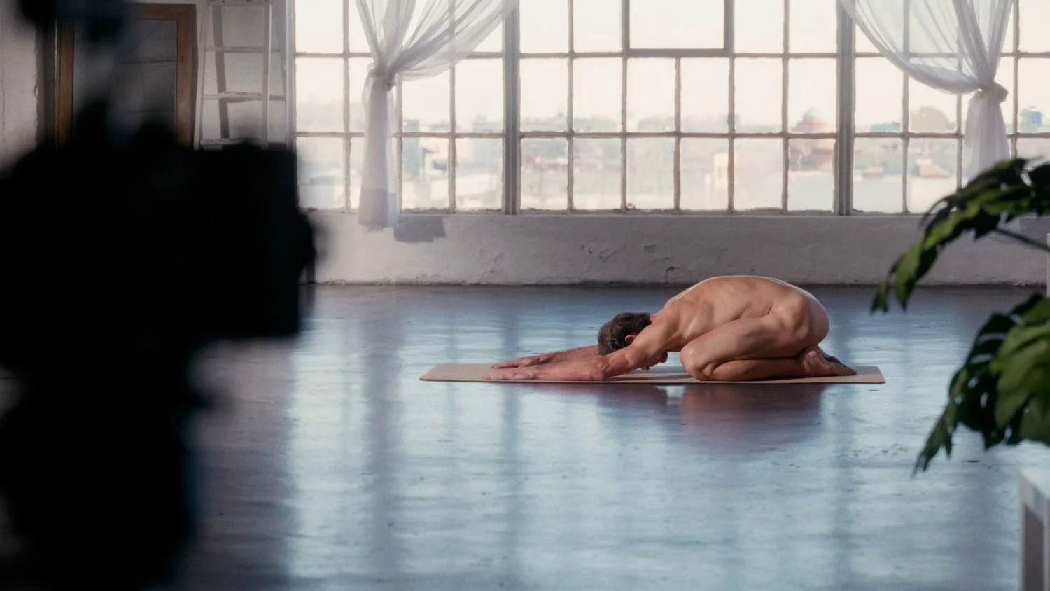 naked man in loft space on a yoga mat in child's pose
