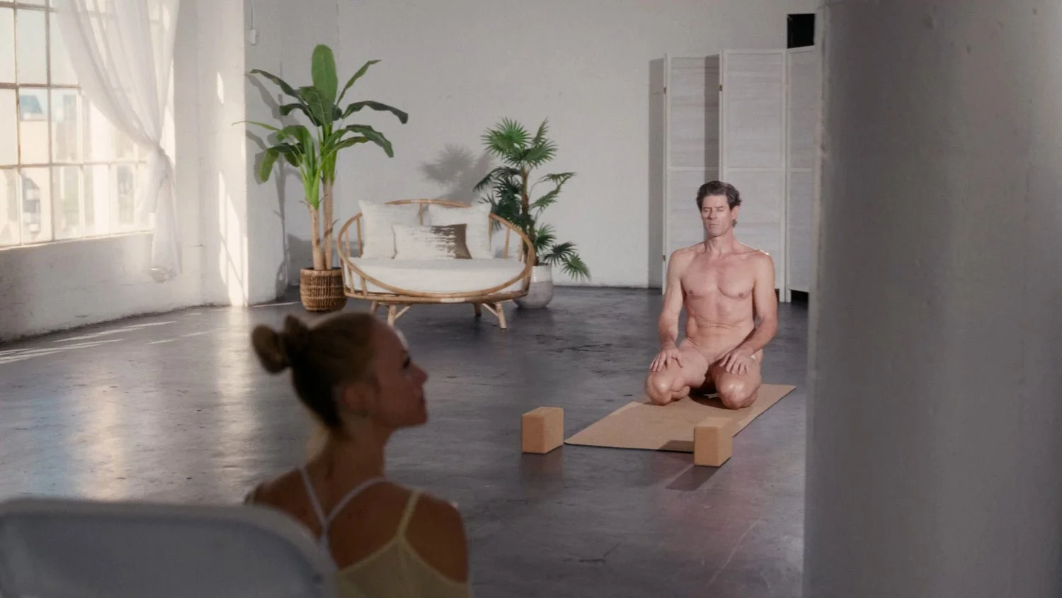 man practicing naked yoga with woman instructor in foreground
