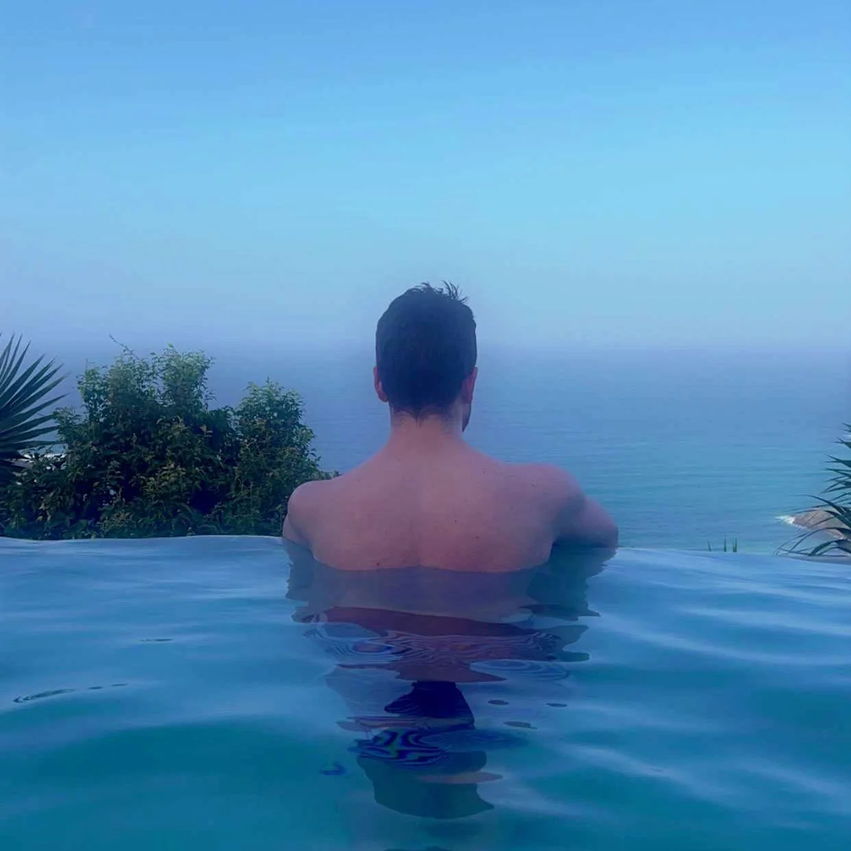 man in tropical location in an infinity pool looking out to horizon