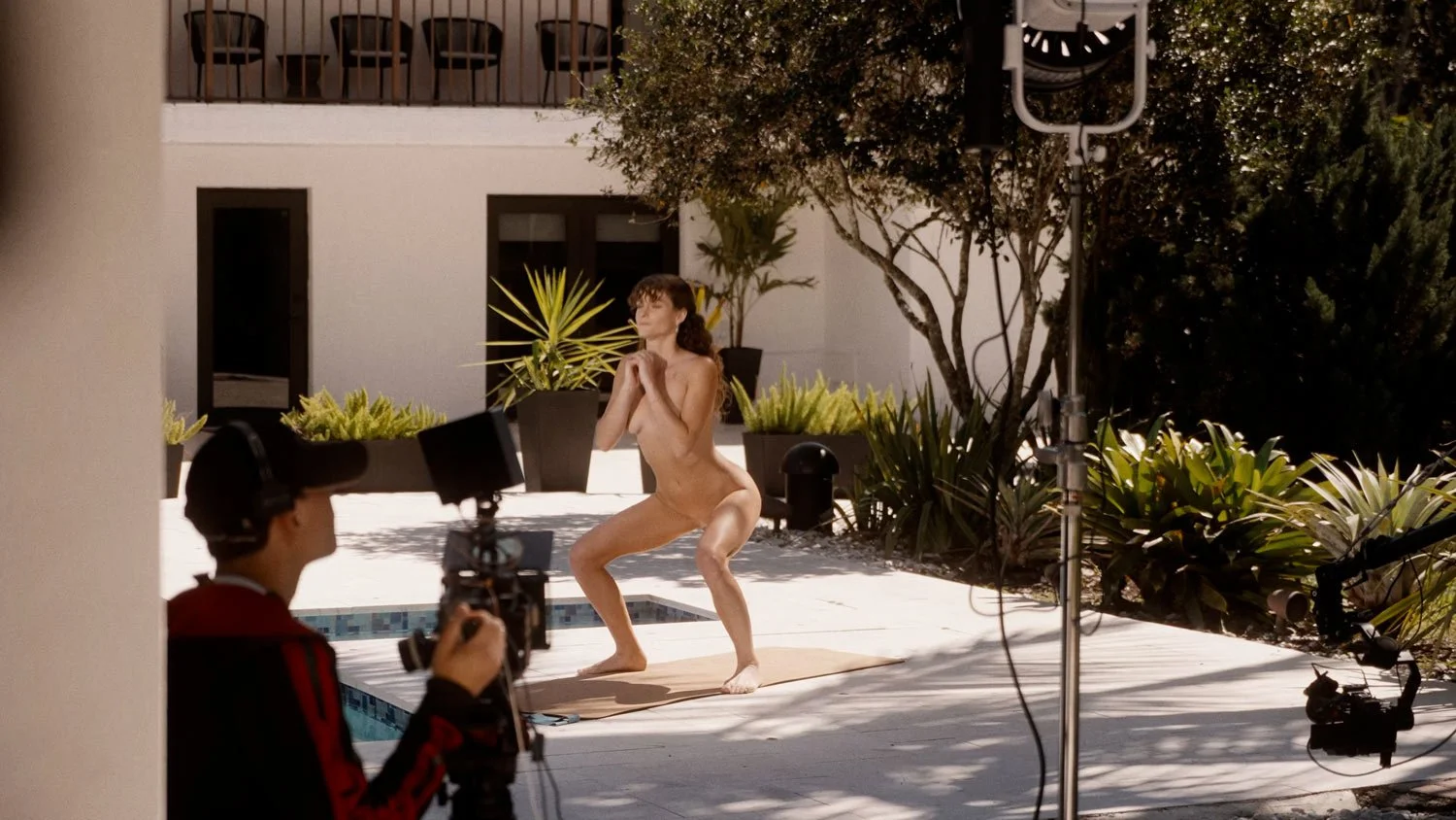 woman being filmed doing squats on set of a naked workout video