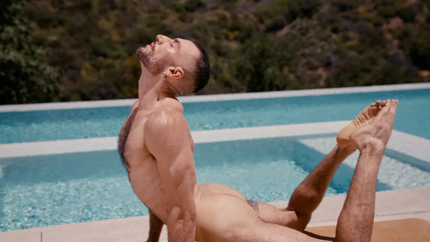 man practicing naked yoga in cobra pose by pool