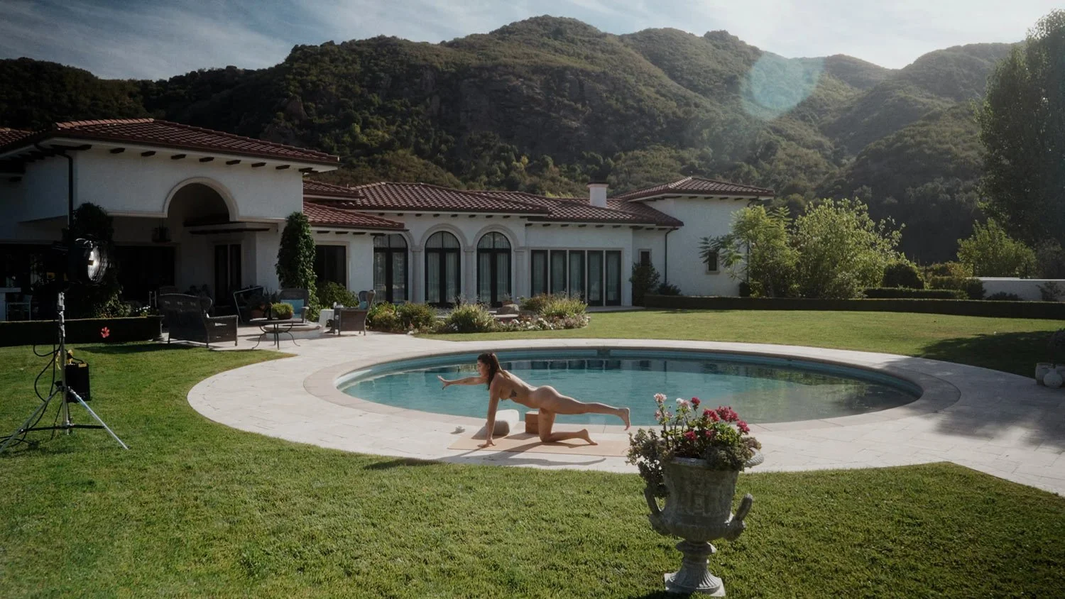 woman doing naked yoga outside with mediterranean villa and mountains in the background