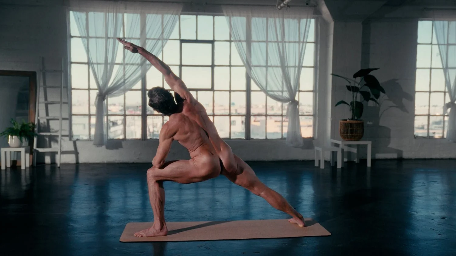 man practicing naked yoga in a loft space in extended side angle pose