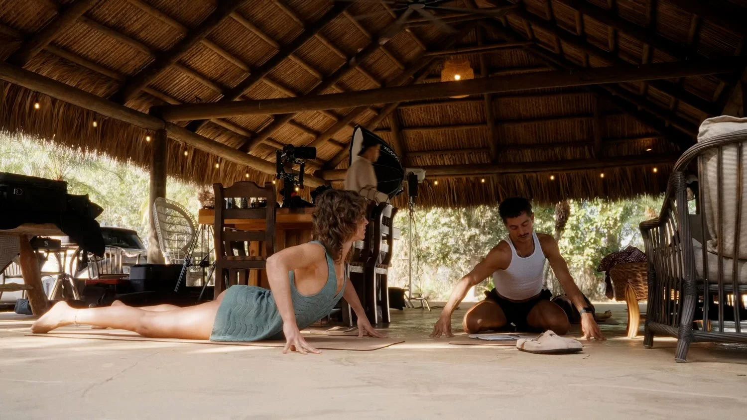 woman and man doing yoga under thatched roof hut