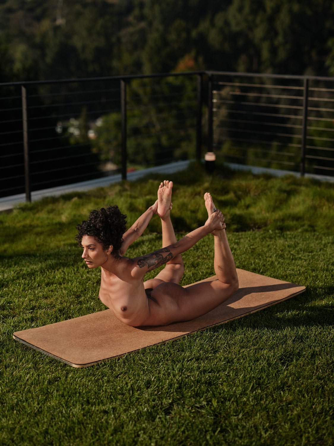 nude woman on yoga mat outside in bow pose