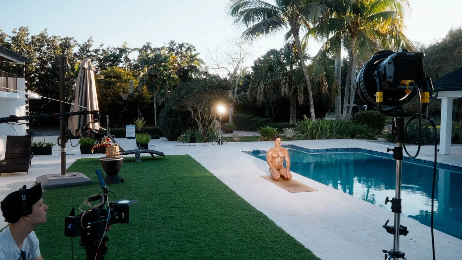 man on a set of a naked yoga shoot in thunderbolt pose by a pool