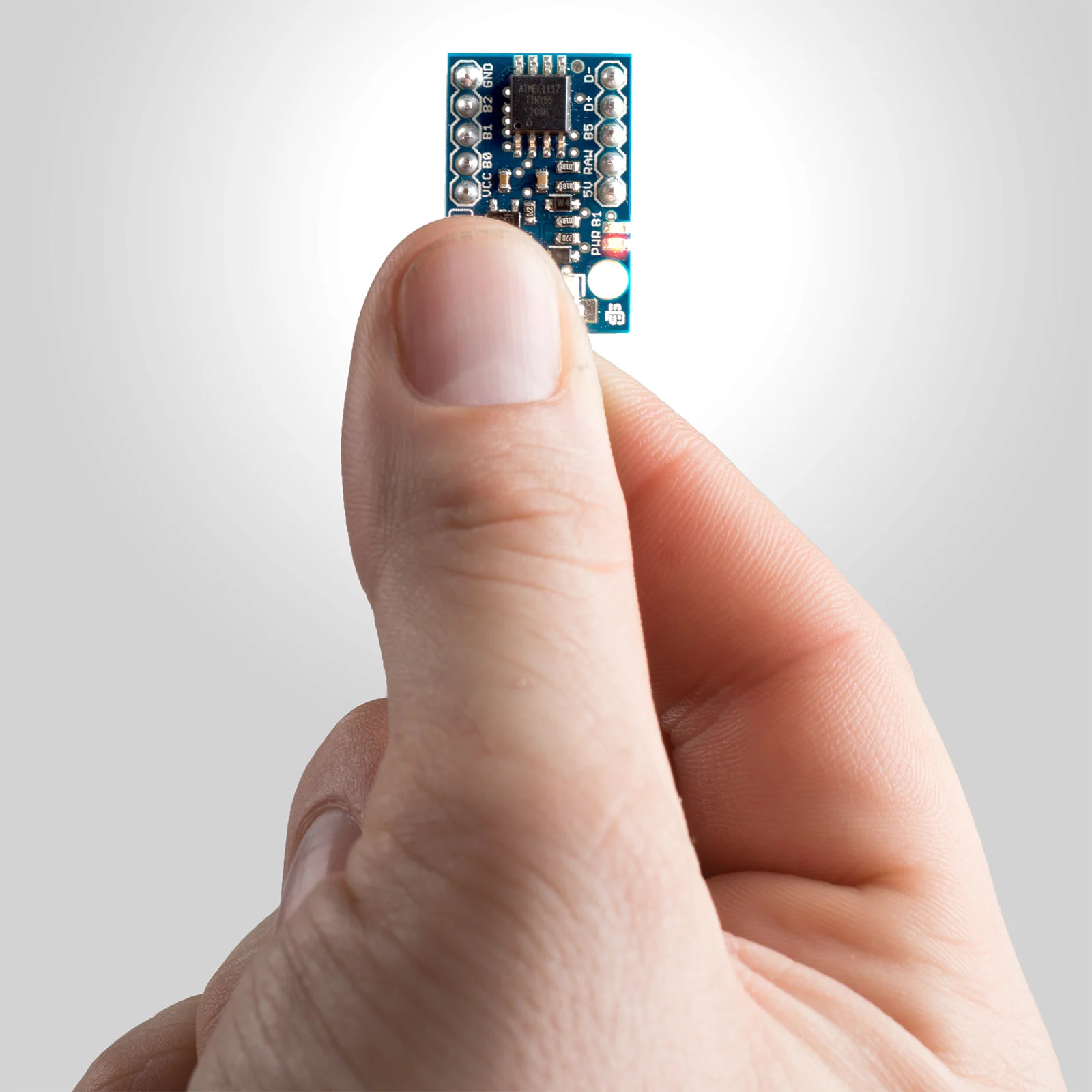Hand holding small circuit board manufactured by Jaycon
