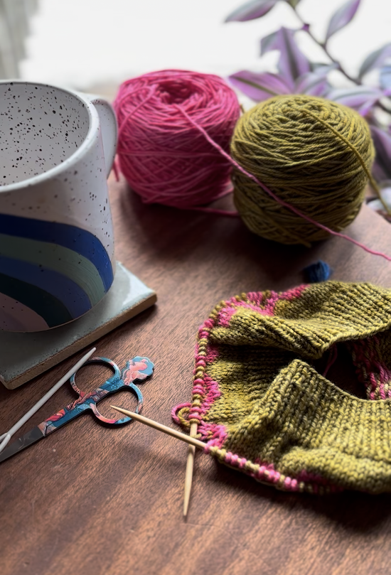 Hand knit hat with coffee mug, yarn, and notions on table