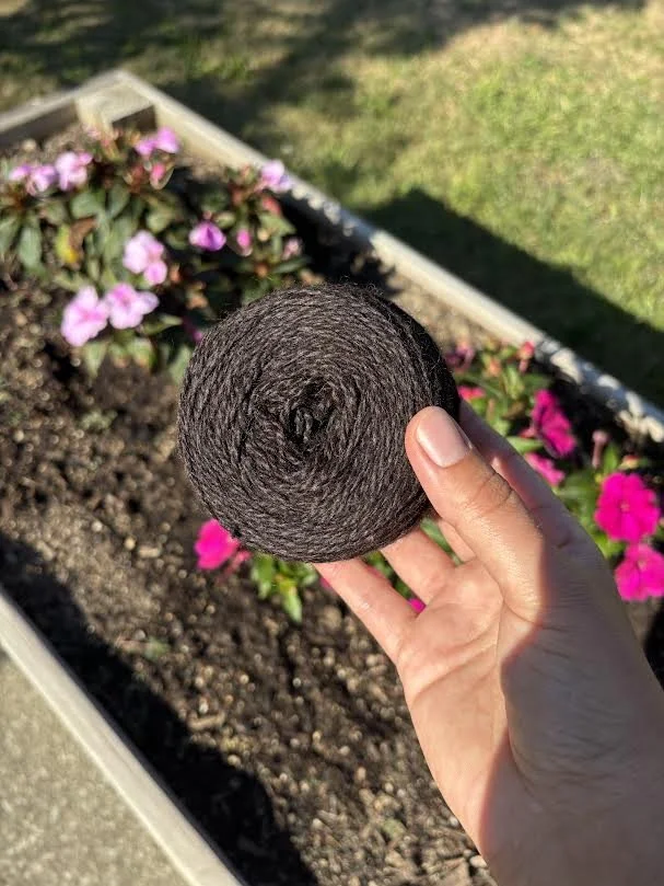 brown yarn being held next to pink flowers