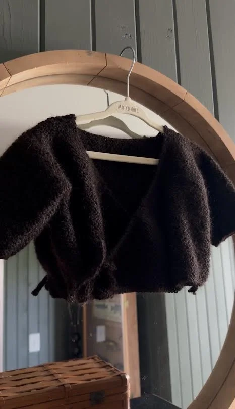 completed baby cardigan hanging on mirror
