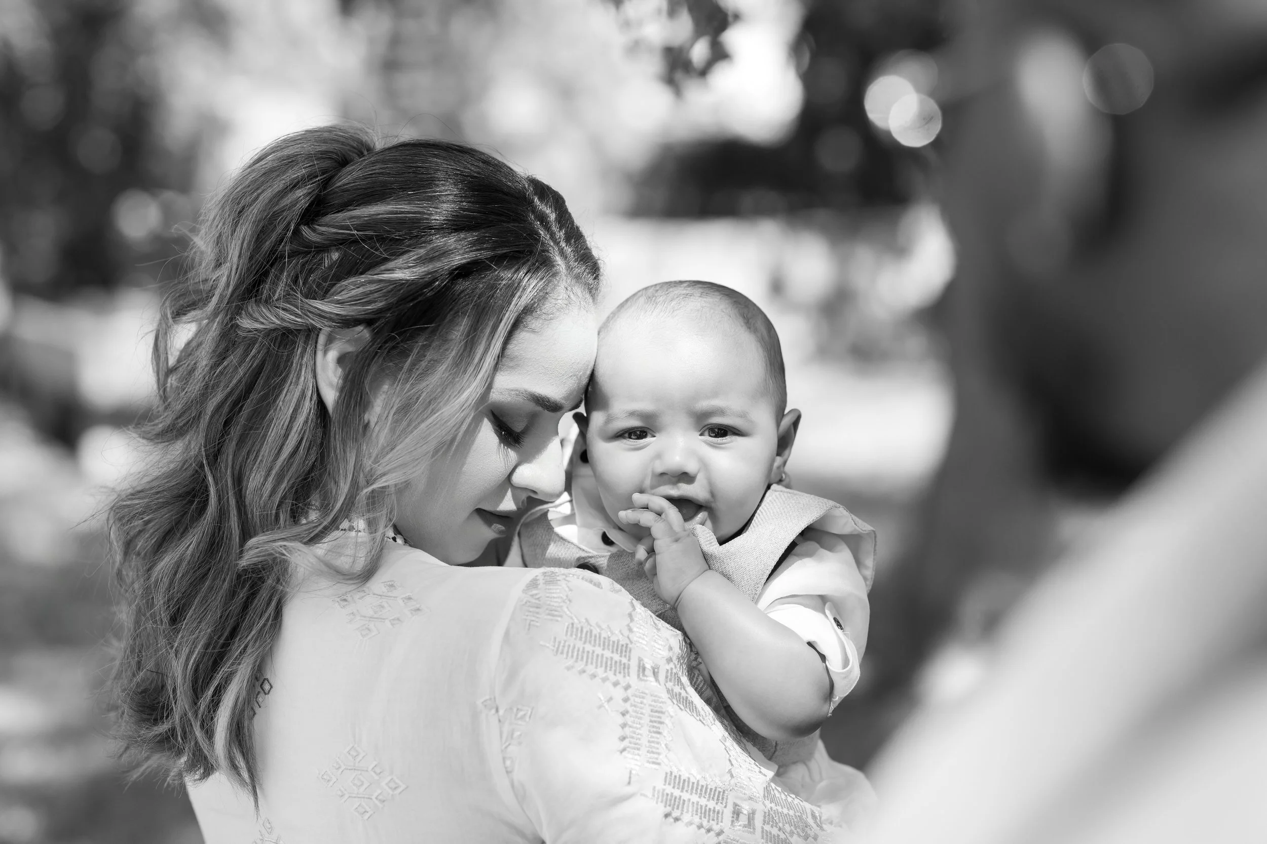 A woman holding a crying baby outdoors, with a person in the background.