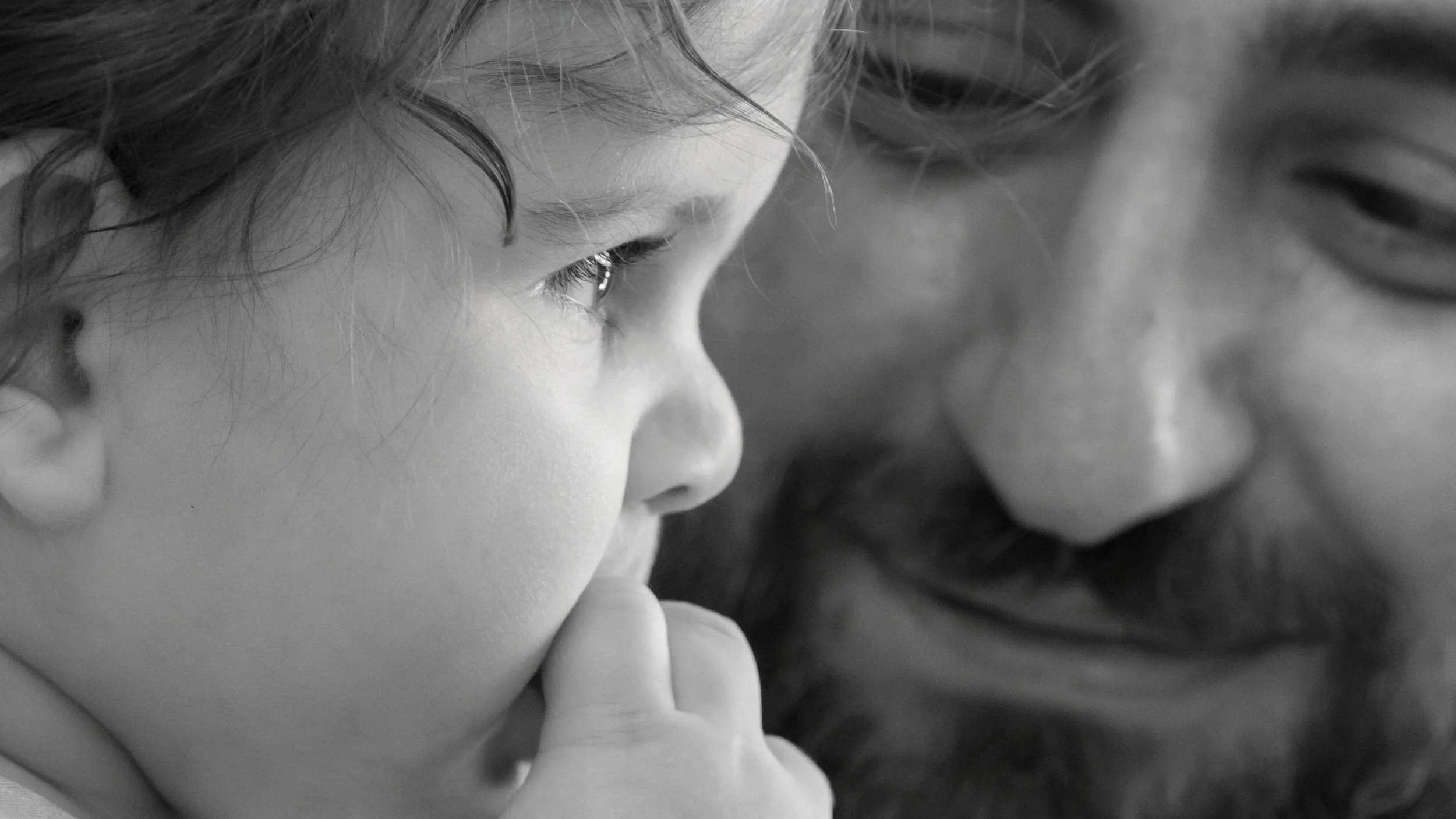 An adult and a child close together, both staring at something with focus, black and white photograph.