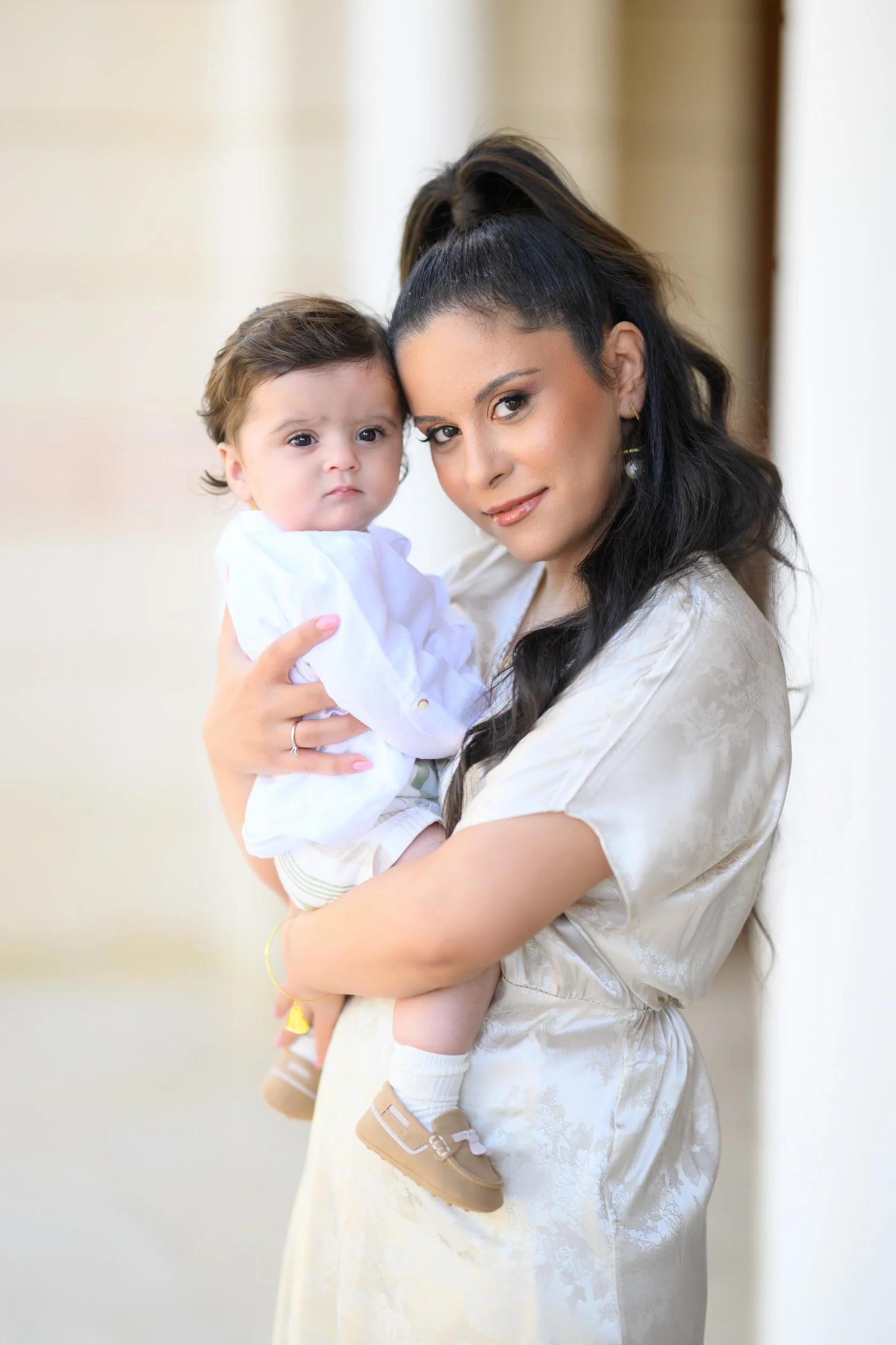 A woman with dark hair holding a young boy with light brown hair against a light background.