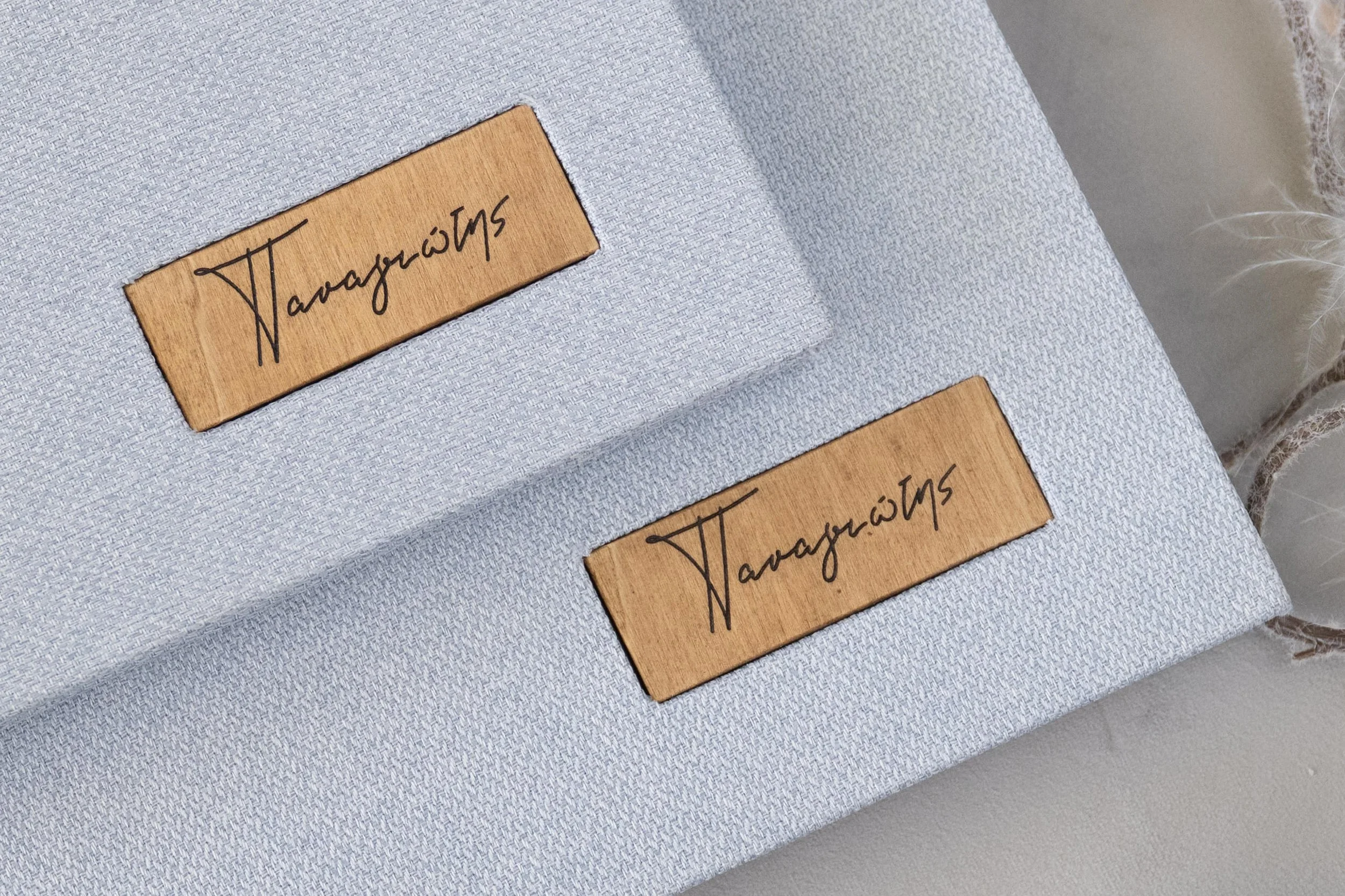 Two wooden name tags with black cursive writing placed on a light gray fabric surface.