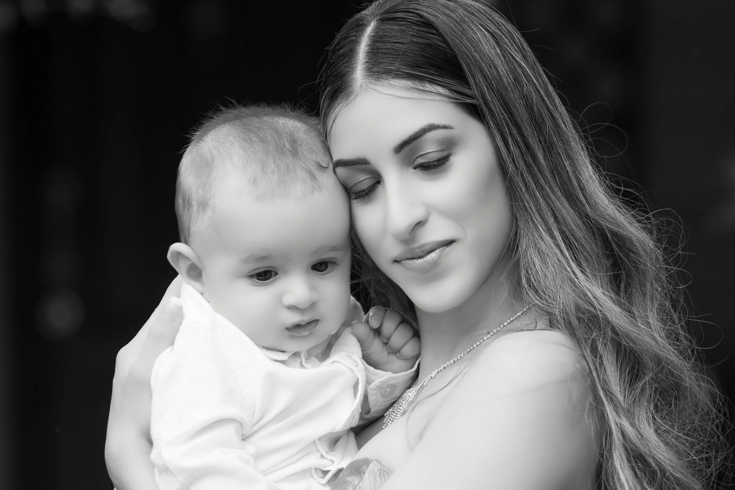 A woman holding a young child close, both with their eyes closed, in black and white photography.
