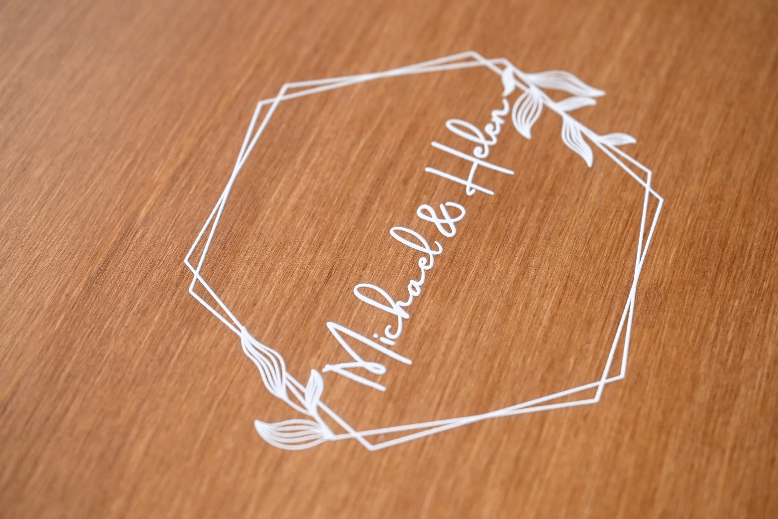 A wooden lay flat album cover with a white decorative frame and the text 'Nicholas & Alexa' written inside.