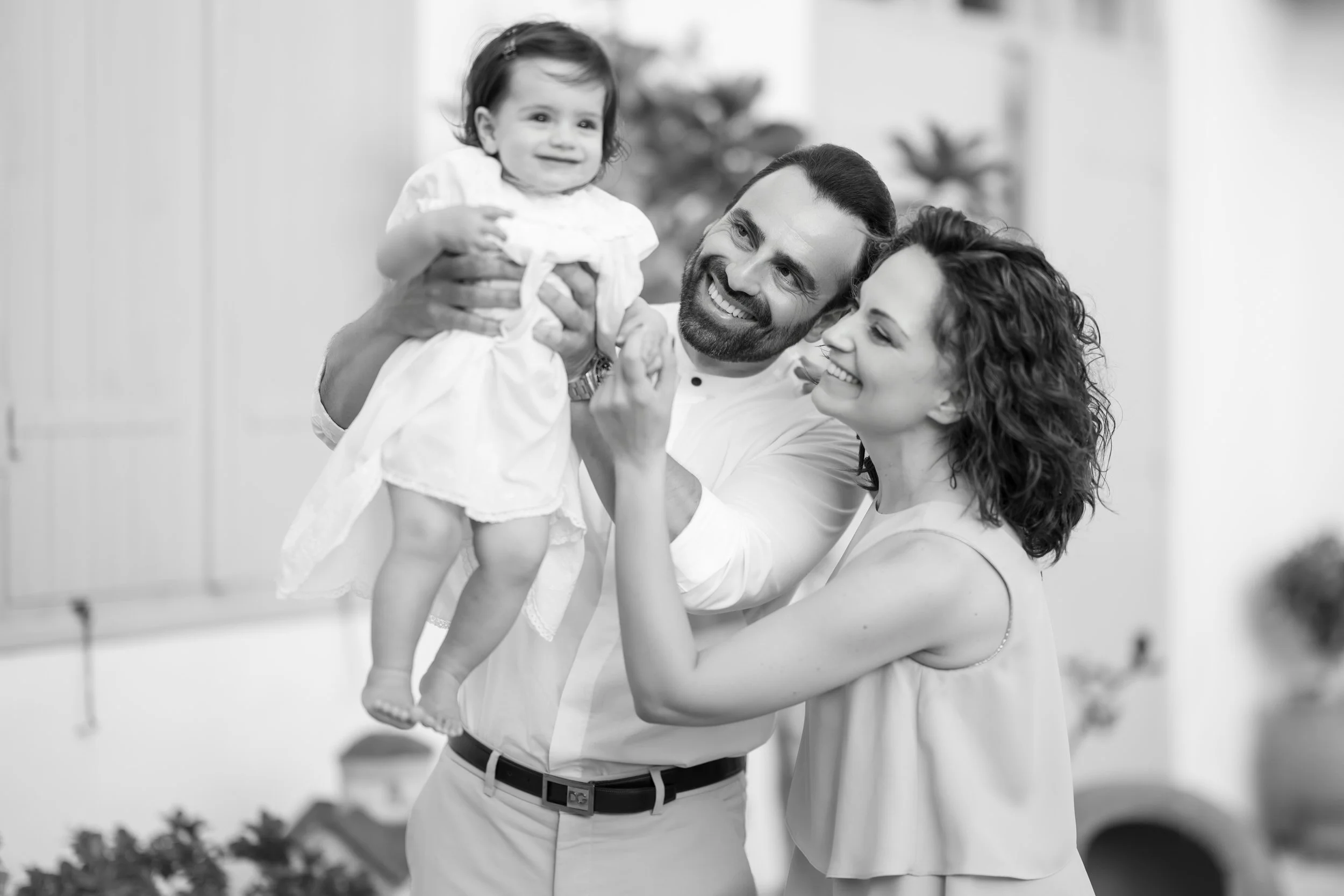 A happy family of three, with a father, mother, and their young daughter, smiling while playing together indoors.