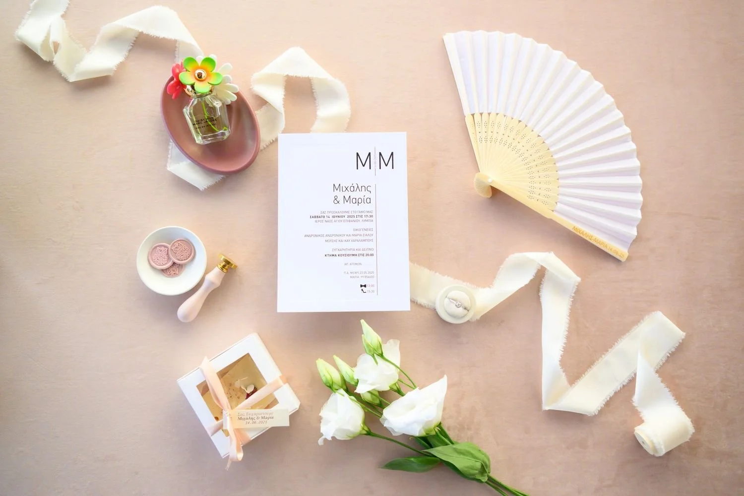 Wedding invitation with flowers, fan, ribbon, and decorative items on a light pink background.