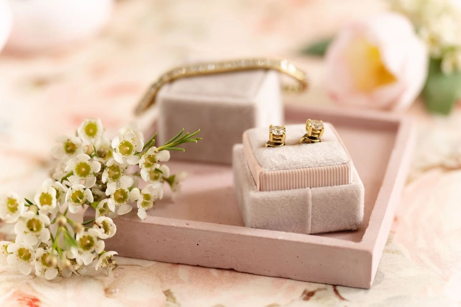 Gold rings in a pink jewelry box, surrounded by white flowers, with a blurred flower in the background.