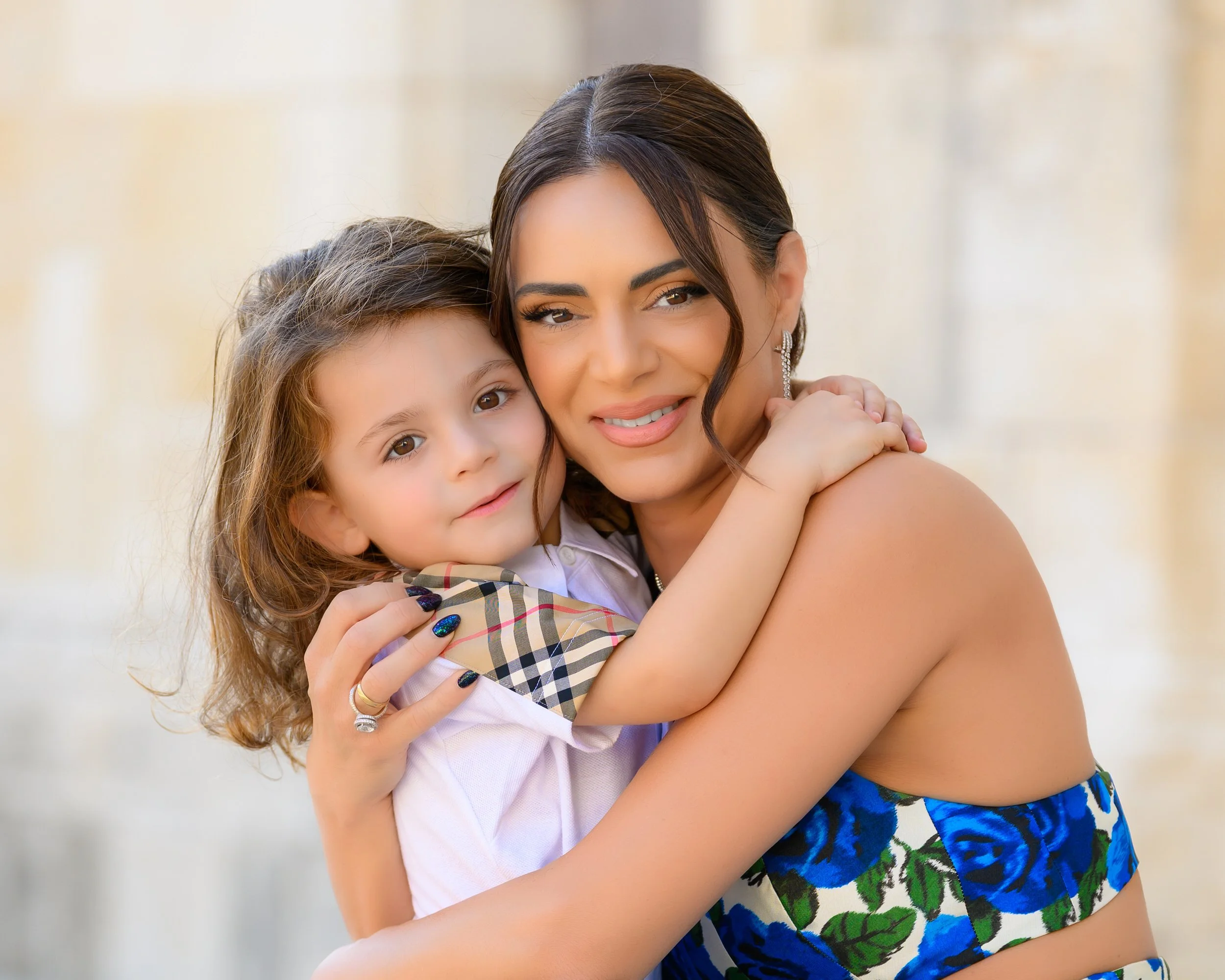 A woman and a young girl hugging and smiling at the camera, with a blurred background.