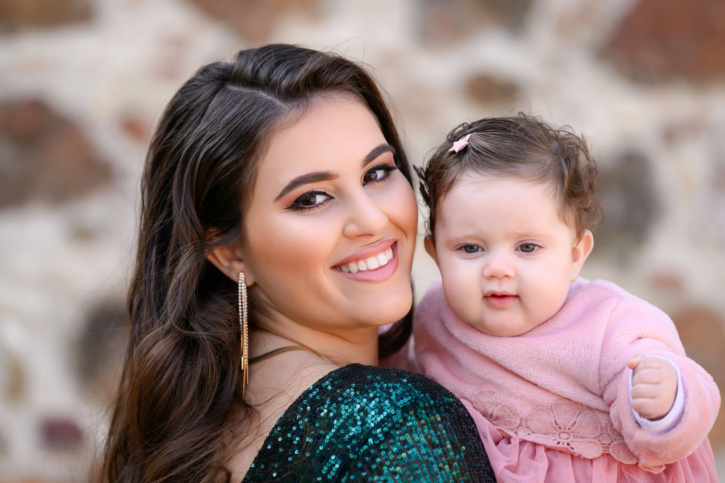 A smiling woman holding a young girl in her arms outdoors with a blurred natural background.
