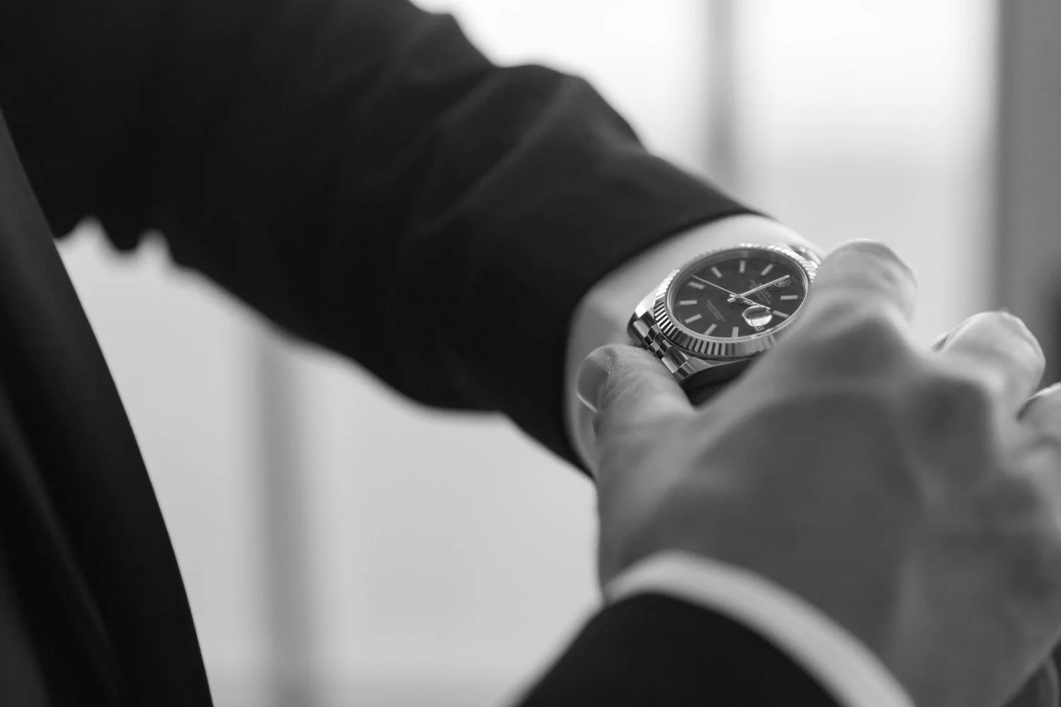 Black and white photo of a person adjusting a wristwatch on their suit sleeve.