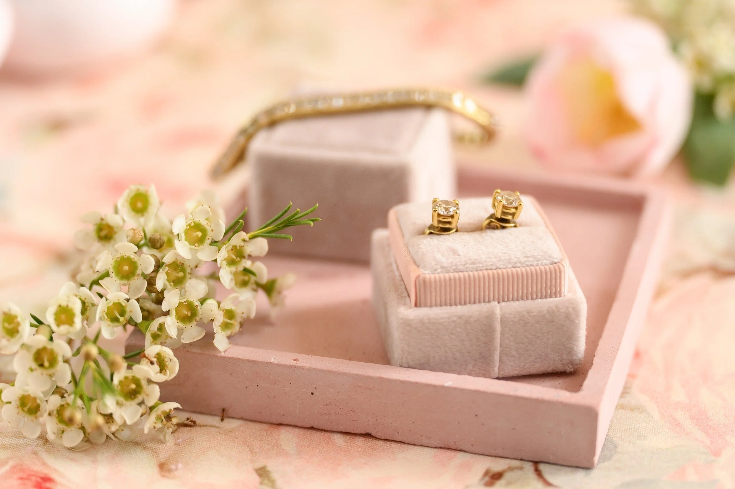 A necklace, a pair of earrings, and a bracelet displayed in a pink jewelry box, with white flowers and pink roses in the background.