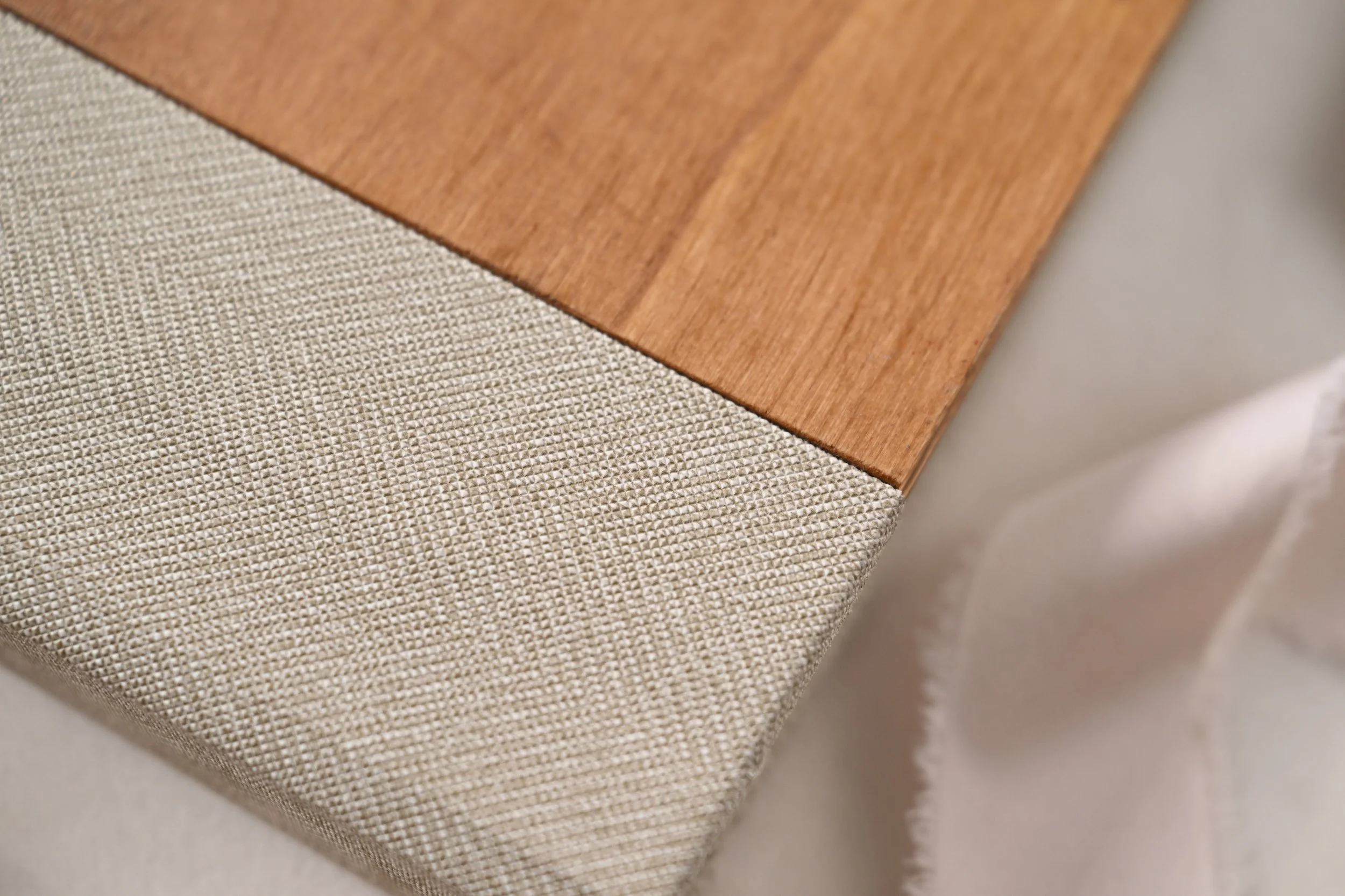 Close-up of a wooden lay flat album  corner with beige, textured fabric upholstery on the edge.