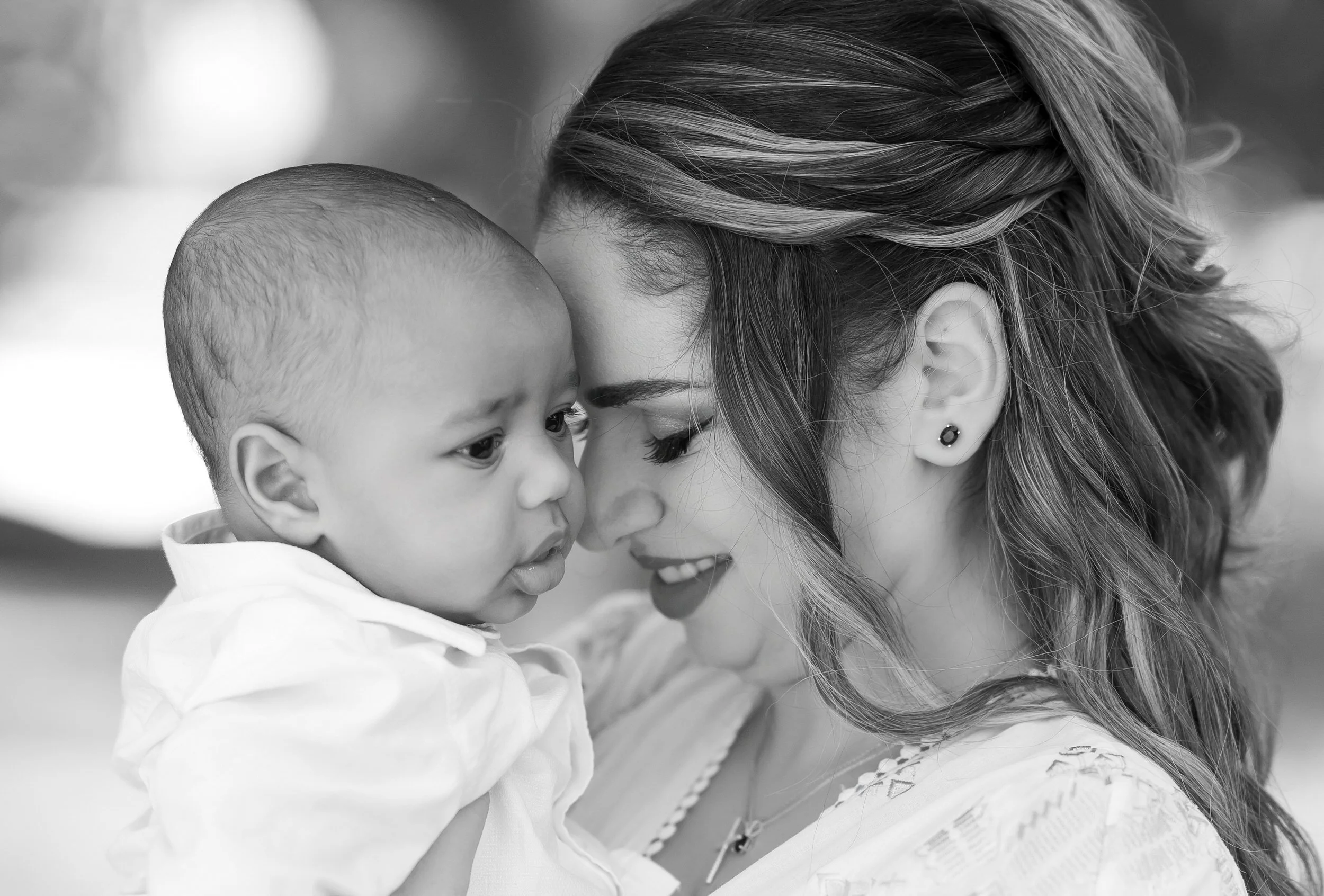 A woman holds a young child close, touching foreheads in a tender moment, both facing each other closely.