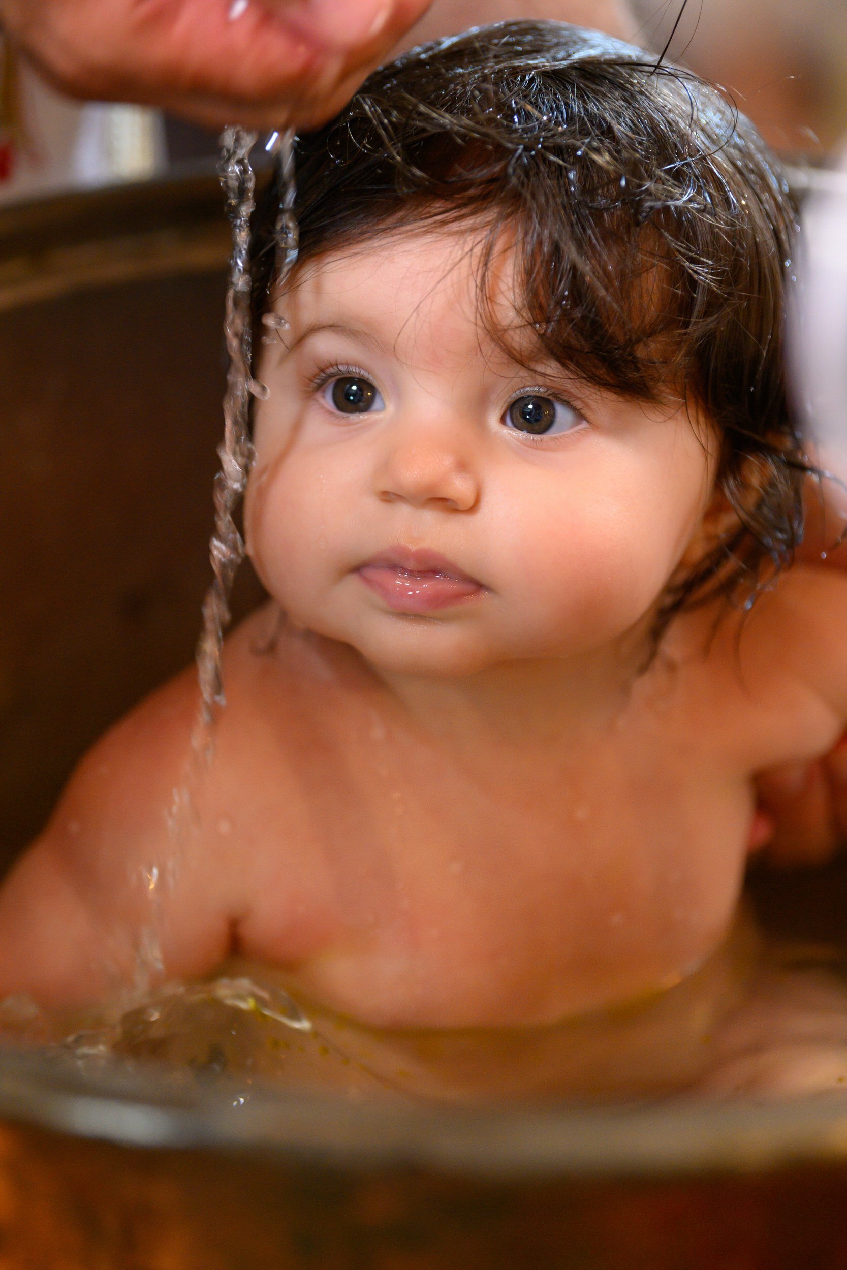 A young child with wet hair is being washed or bathed, with water pouring over their head.