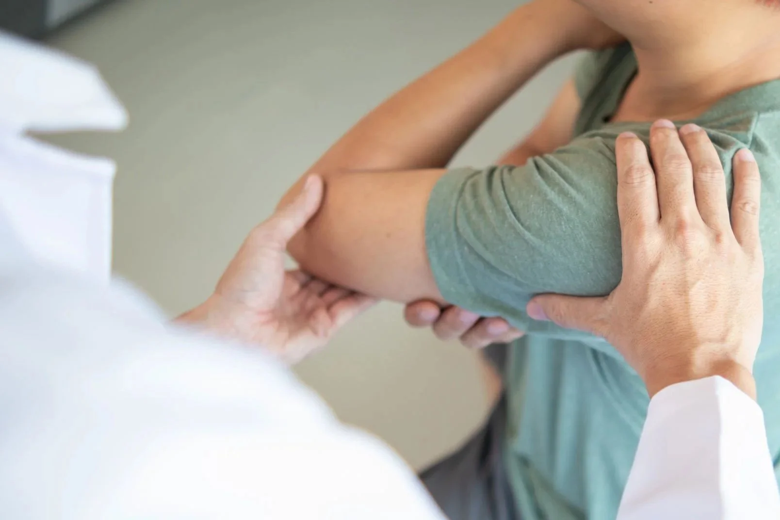 A chiropractor examining a patient's shoulder, with one hand on the patient's upper arm and the other on the shoulder.