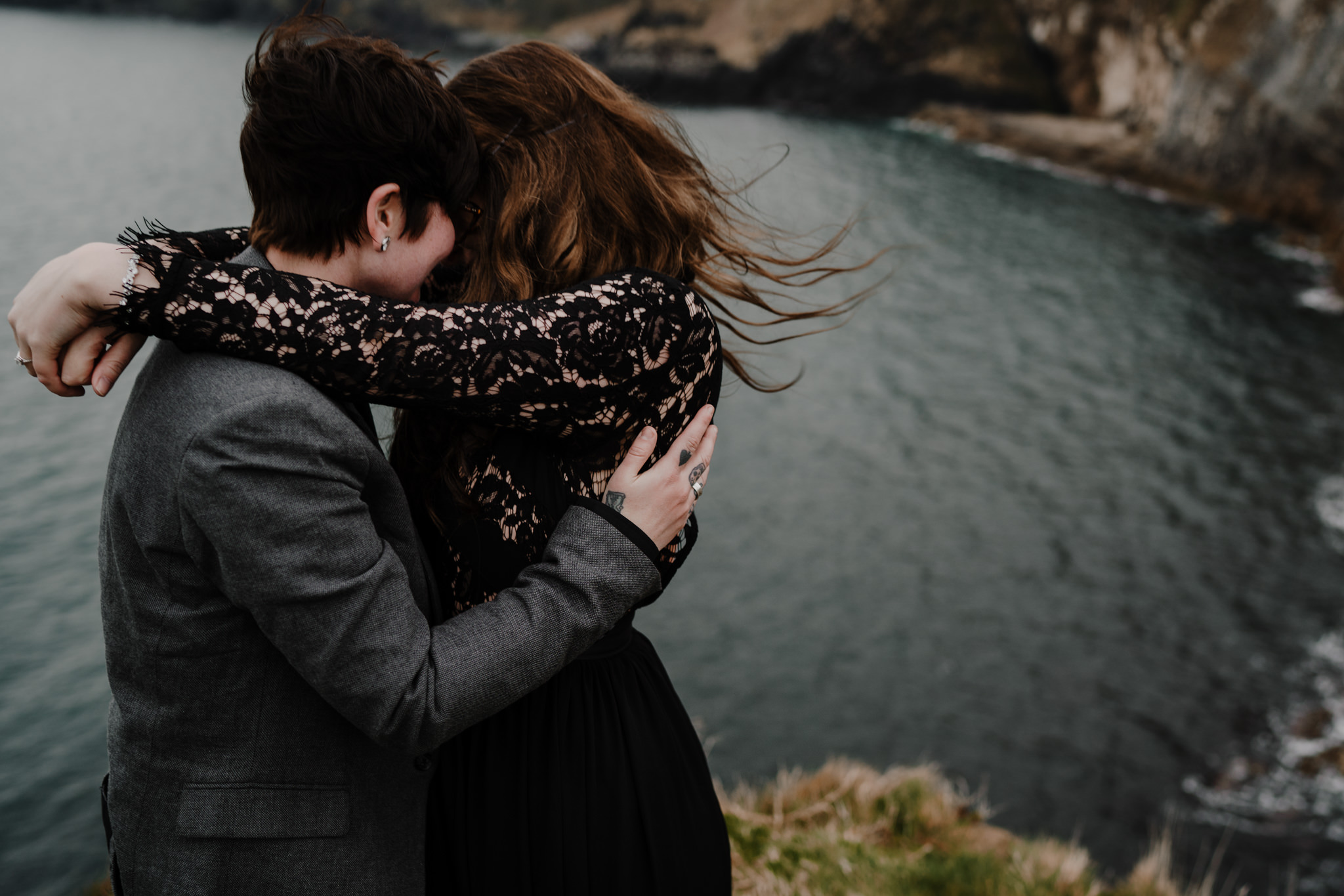 LGBT couple embrace cliff edge windswept Kinbane castle adventure engagement proposal