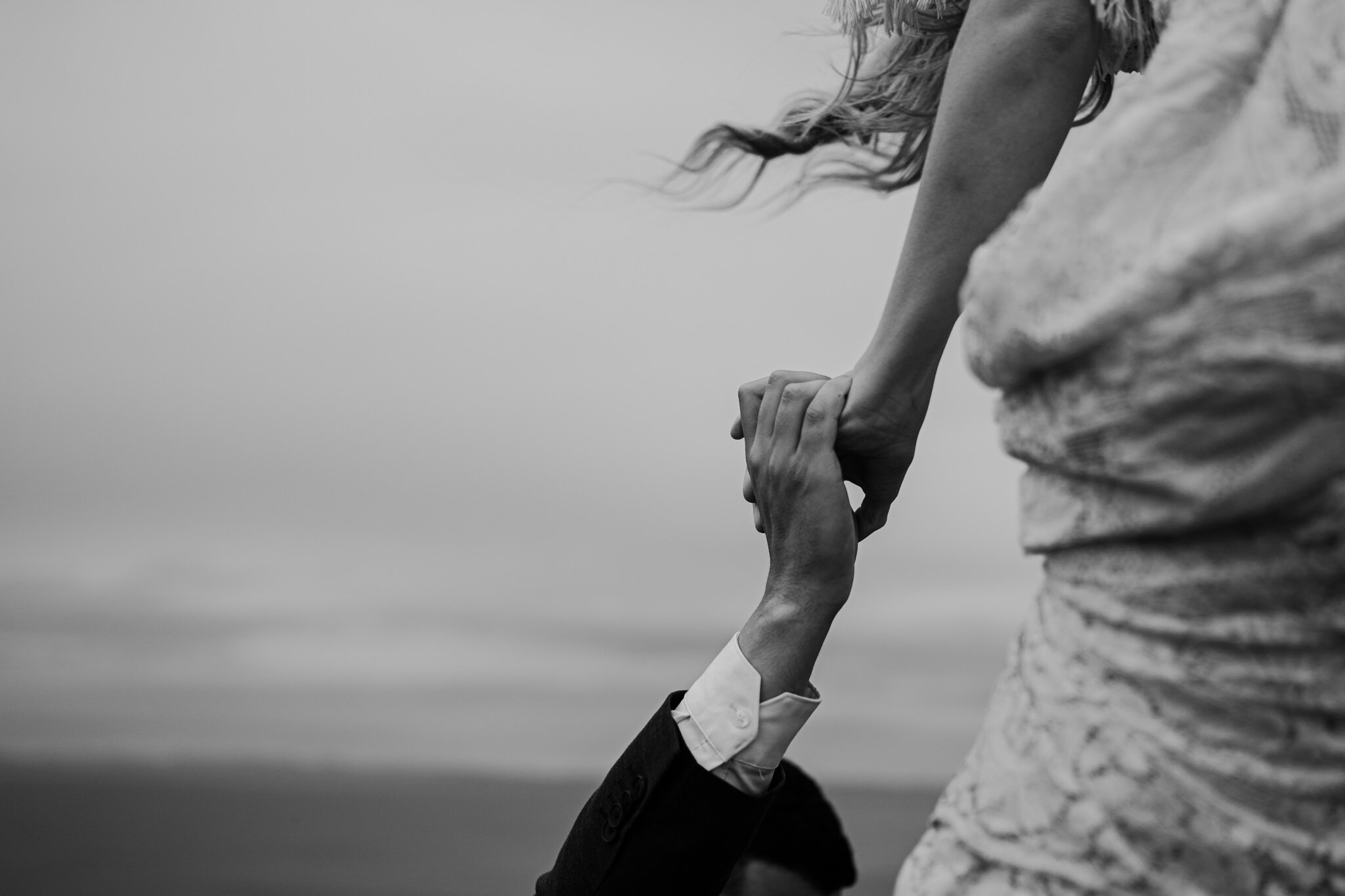 bw closeup husband helps wife over fence at cliffs of moher adventure elopement