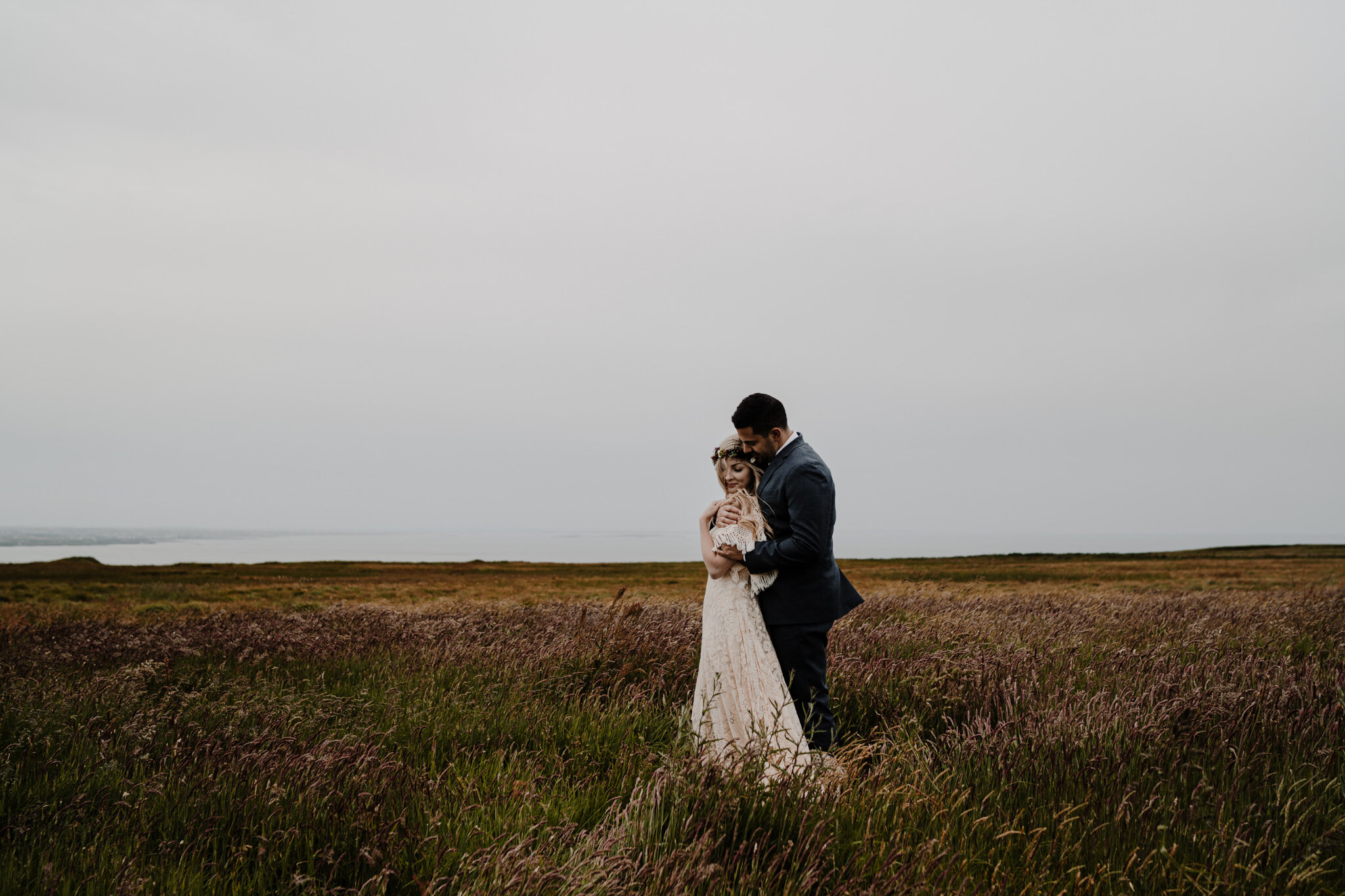 husband and wife stand in irish field hugging at cliffs of moher adventure elopement