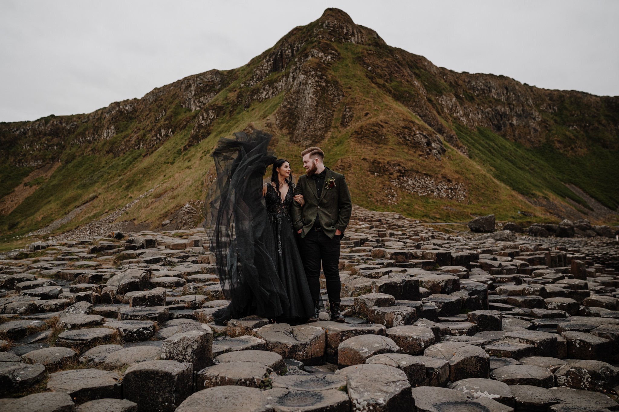  alternative American couple elope in northern ireland at the giants causeway in a black wedding dress and tweed suit 