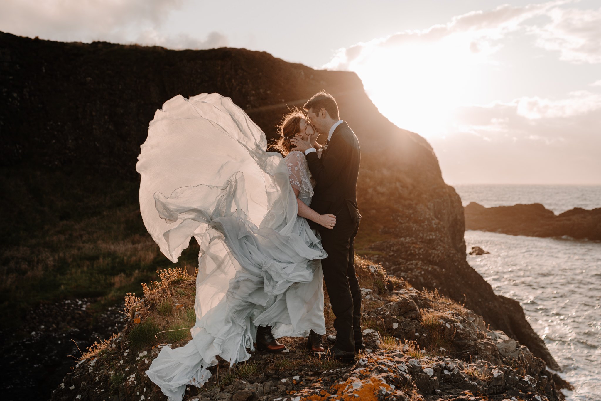  couple kiss while brides leanne marshall dress flows in the wind during their fairytale northern Ireland elopement 