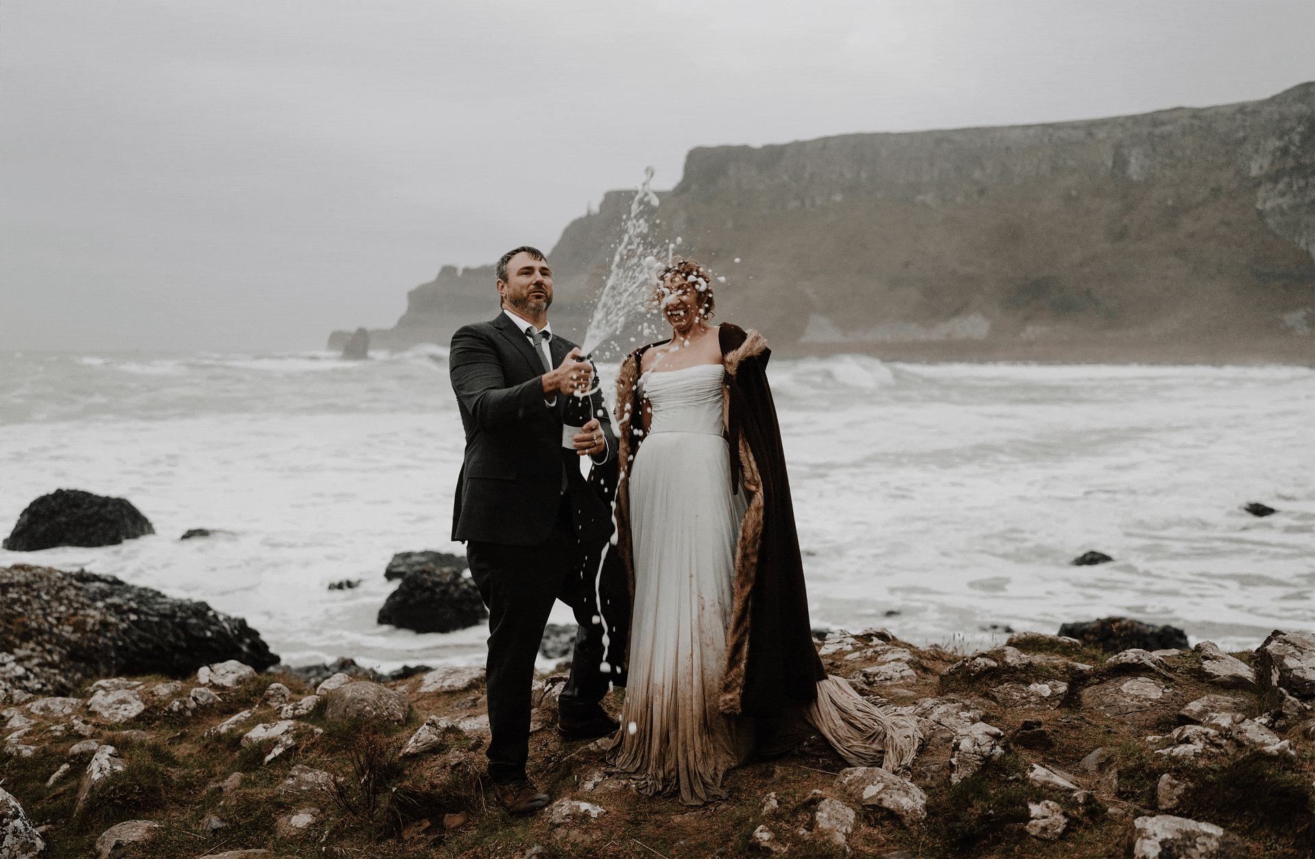 couple celebrate their elopement with a champagne pop at the giants causeway in winter