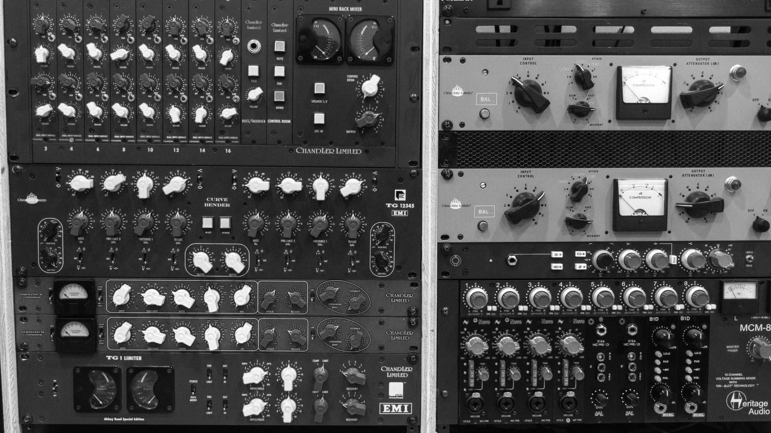 Close-up of a professional audio mixing and recording rack with various audio equipment and controls, including knobs, meters, and switches. Chandler pieces include the Curve Bender, TG1, Germaniums, Mini Rack Mixer, and RS124.