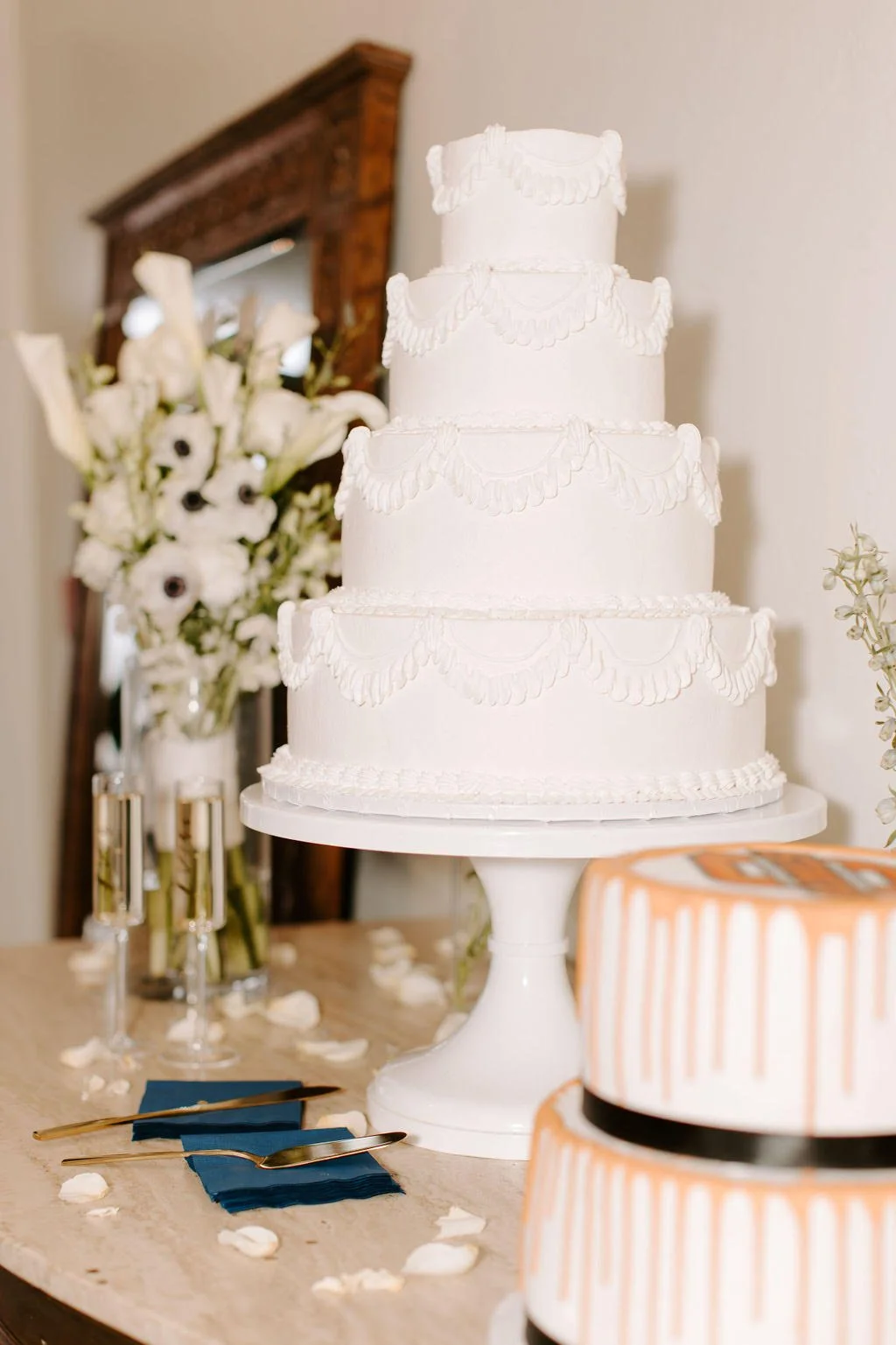 A three-tiered white wedding cake with decorative icing, placed on a white cake stand at a celebration table.