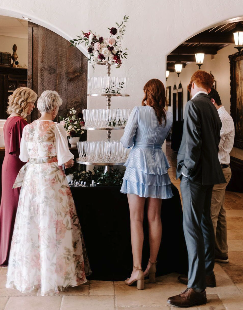 People celebrating at a wedding, serving champagne from a tiered tower with glasses.