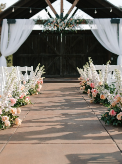 Outdoor wedding ceremony site with white drapes, floral arrangements, and a wooden arch