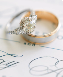 Close-up of a diamond engagement ring and a wedding band resting on a handwritten letter or note.