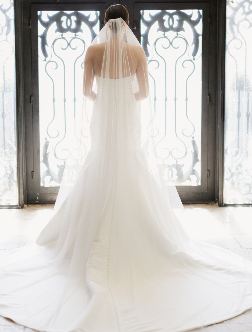 Back view of a bride in a white wedding dress with a long train, standing in front of ornate iron gates.