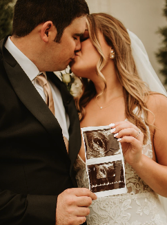 Bride and groom kissing with a sonogram image, during a wedding celebration.