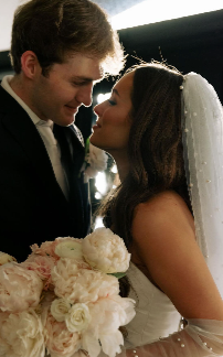 A bride and groom close-up, smiling at each other, with flowers in the foreground, during a wedding ceremony.