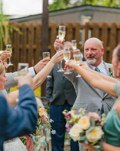 People raising glasses of champagne and wine in a toast at an outdoor wedding celebration.