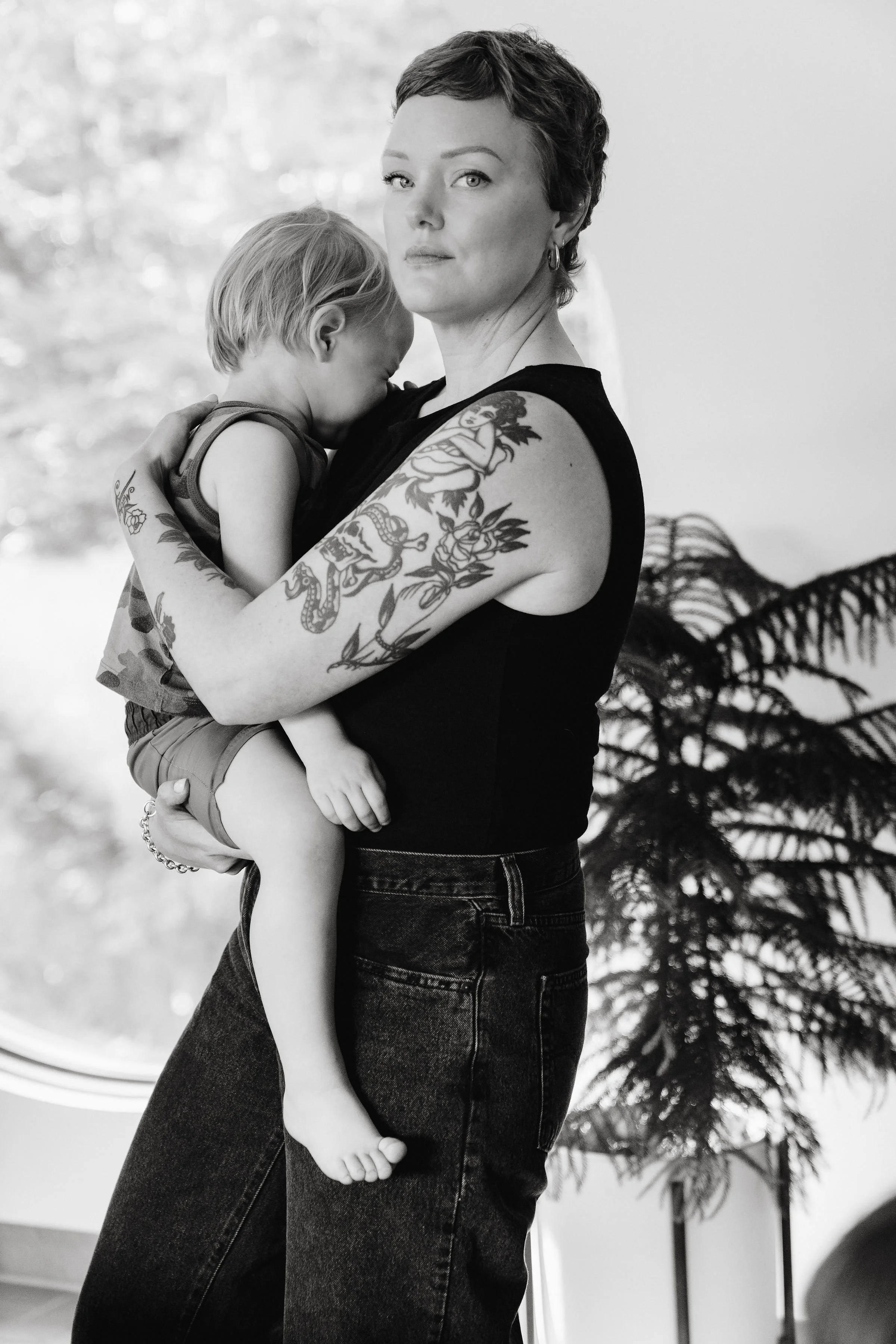 Tina protectively holding her preschool aged son who is crying and looking into the camera