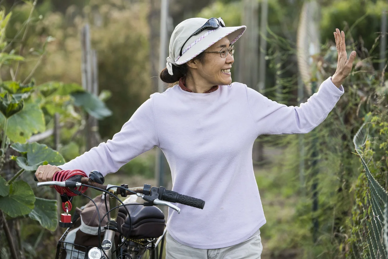  Long-time community gardener Shoko Igarashi waves goodbye to friends while wheeling her bike from her plot at the West Side Community Gardens in Athens, Ohio. 