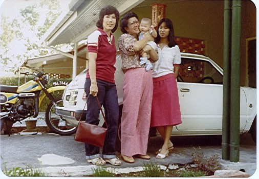 Pictured from left to right: My mom, my grandma holding a baby me, and I’m not sure who that is on the right! All standing in front of an old school looking white car and a yellow motorbike, in suburban Malaysia